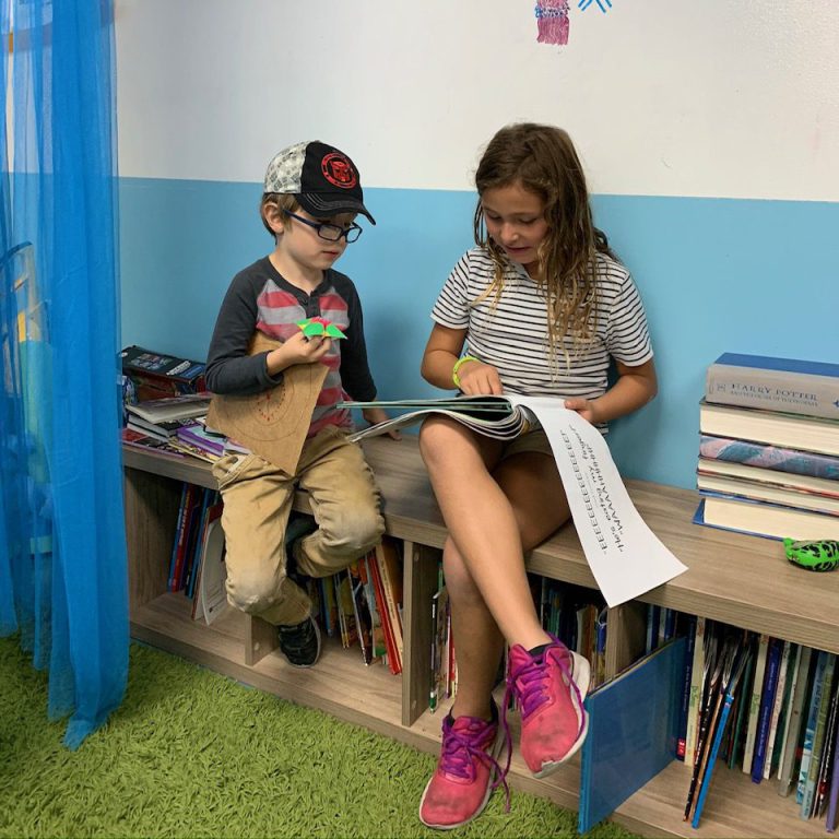 boy and girl sitting on book shelf reading to each other