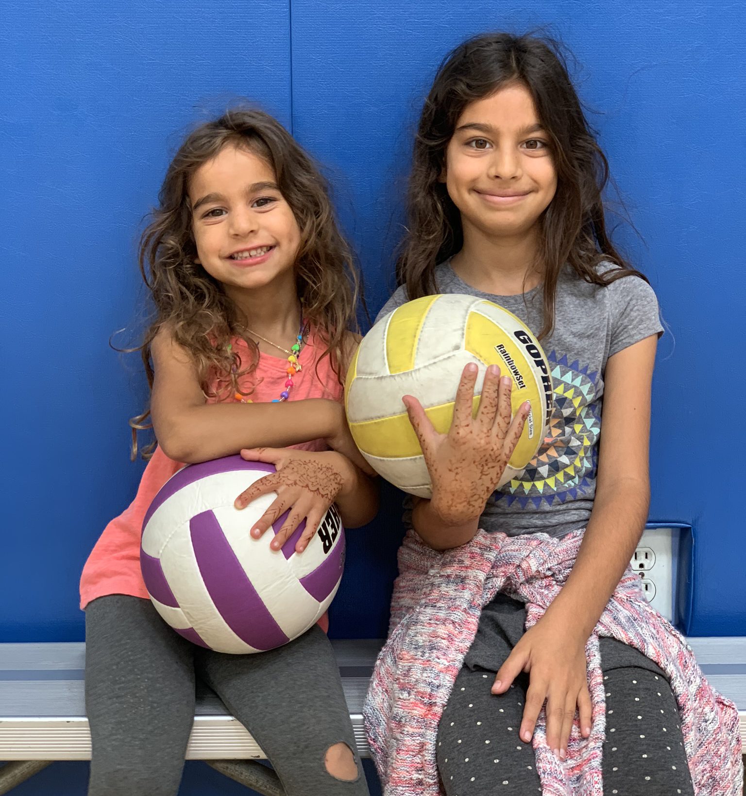 2 girls with volleyballs on bench in gym