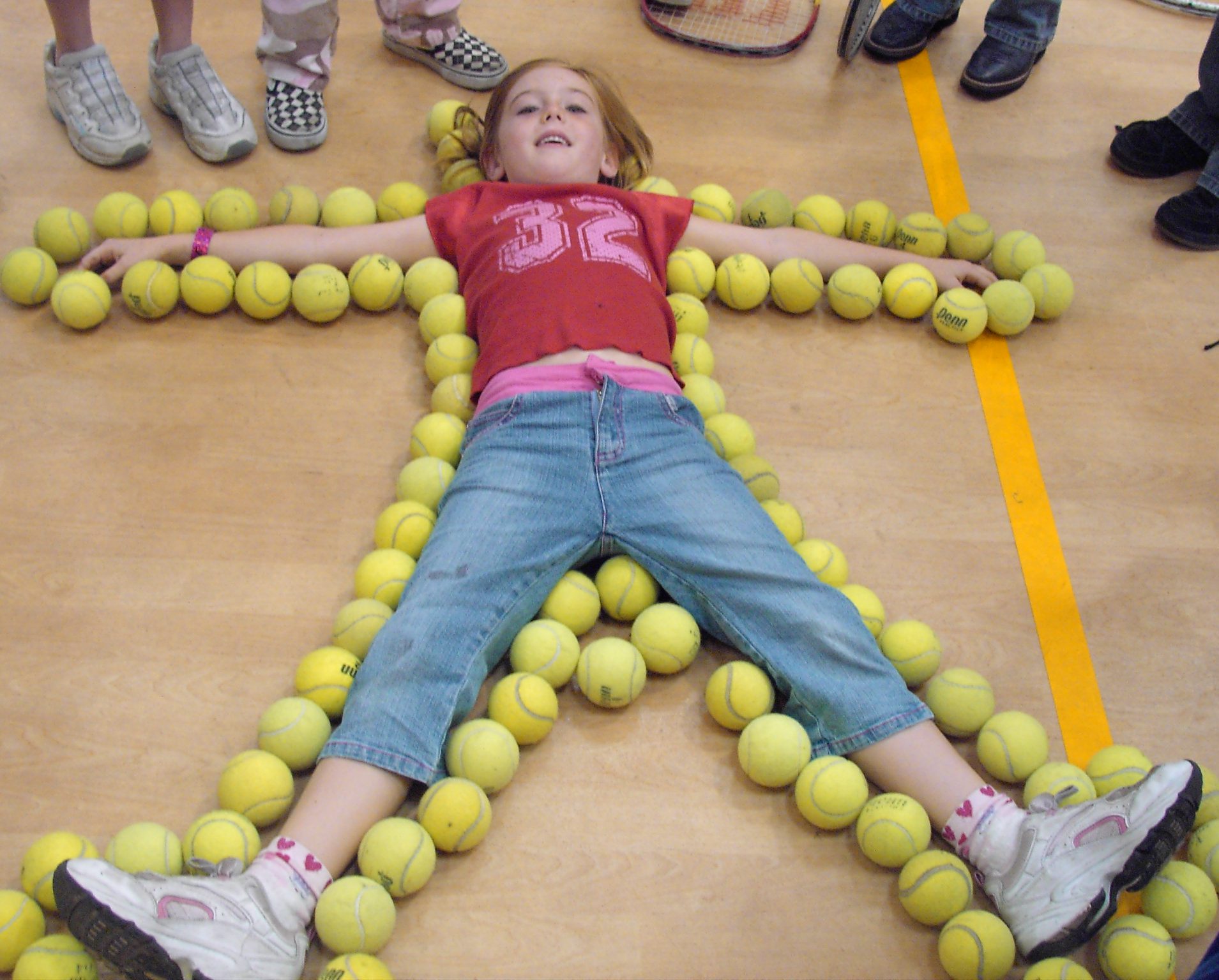 Girl lying flat with arms and legs spread out on floor outlined with tennis balls