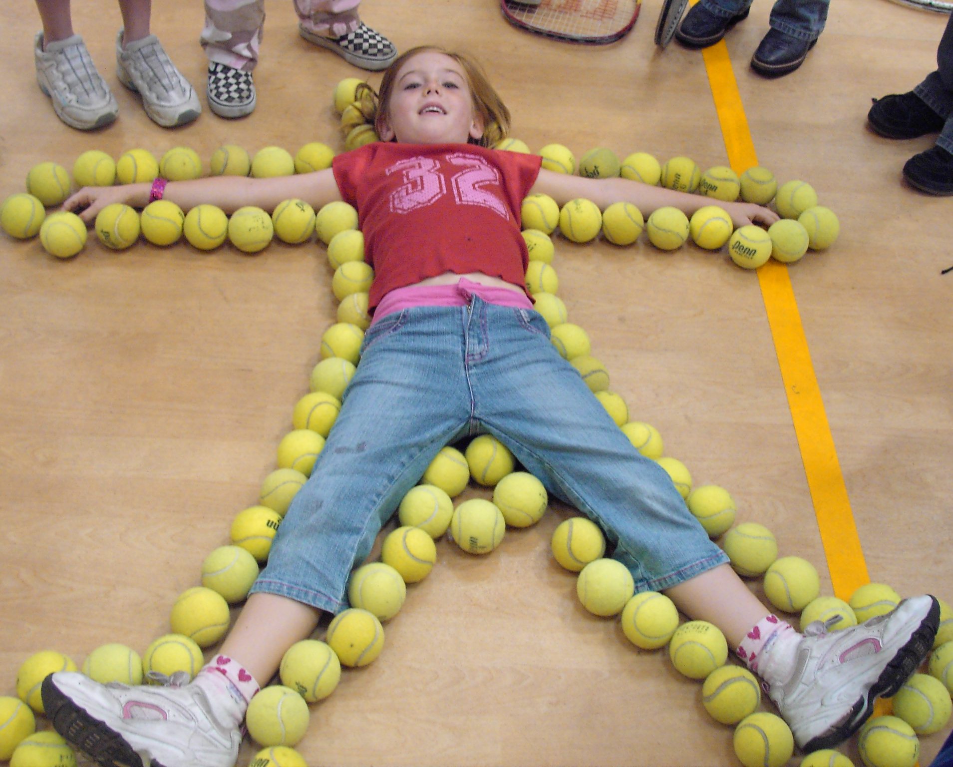 Girl lying flat with arms and legs spread out on floor outlined with tennis balls