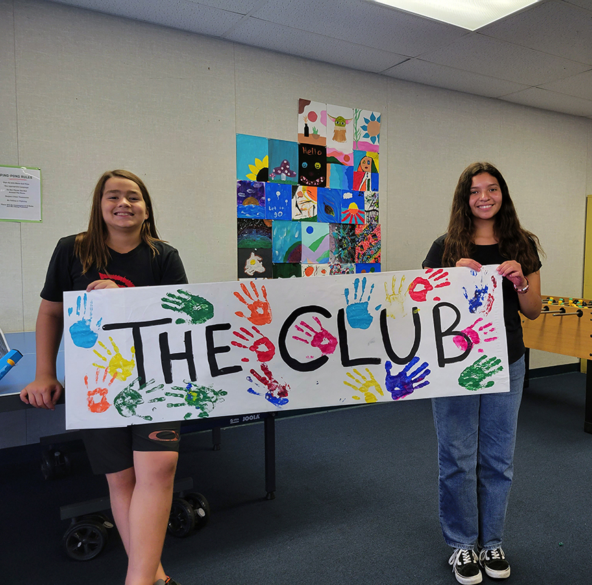 2 middle schoolers hold a handmade sign saying "The Club"