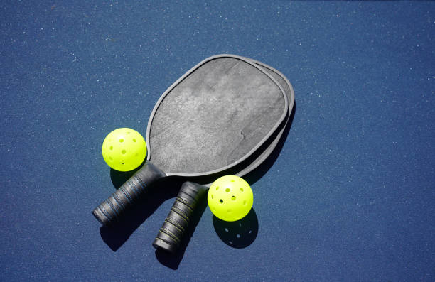2 pickleball paddles on the ground with 2 pickleballs