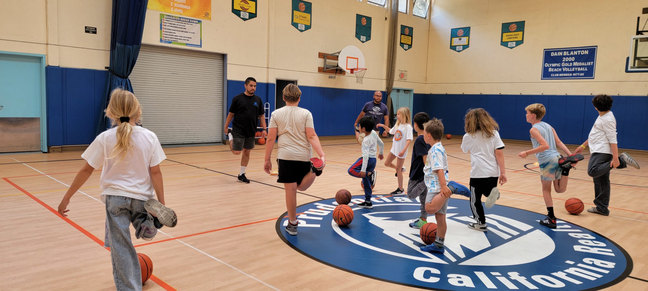Kids stretching on a basketball court during a supervised gym activity.