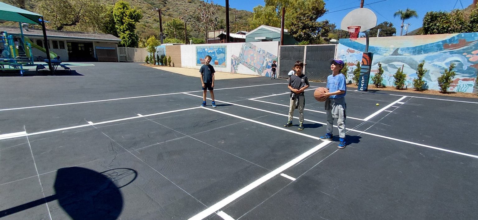 Kids playing basketball on outdoor court at Boys and Girls Club play yard